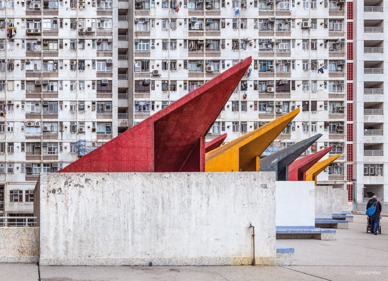 Colourful geometric sculpture with red and yellow angular forms in front of a densely packed Hong Kong residential tower block