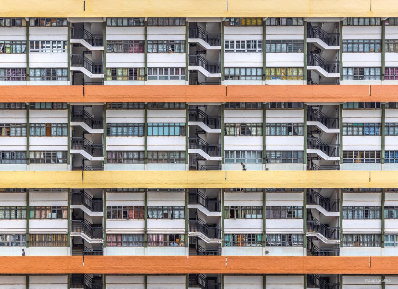 Facade of Choi Hung Estate showing repetitive grid of small windows, curved stairwells and colourful horizontal bands of orange and yellow across the brutalist concrete structure