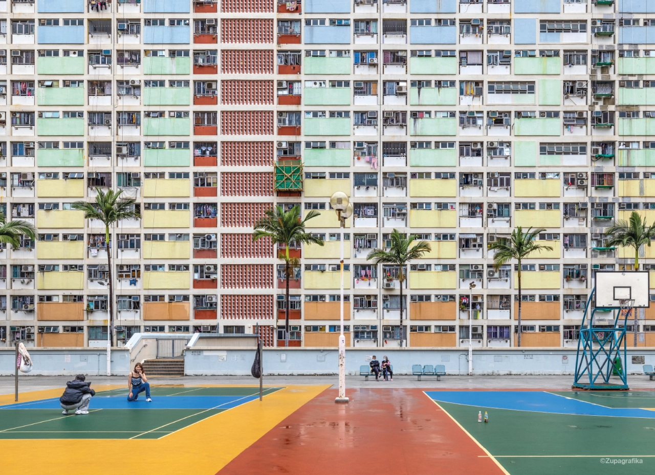 Colourful public housing tower blocks with multicoloured facades in Hong Kong, with a wet basketball court and palm trees in the foreground