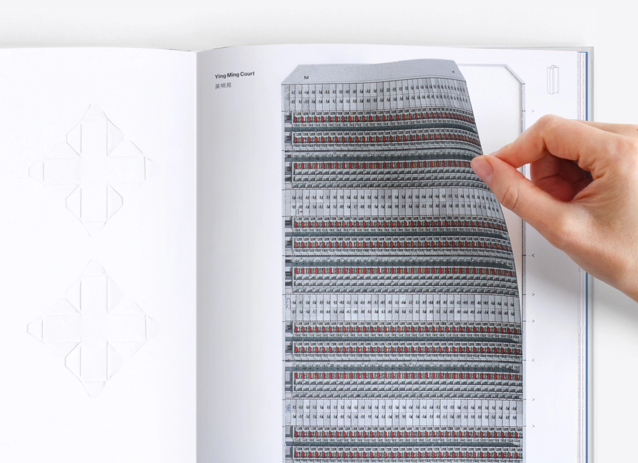 Hand holding open a page of Concrete Hong Kong book revealing a foldout architectural model with geometric patterns in grey, red and black stripes